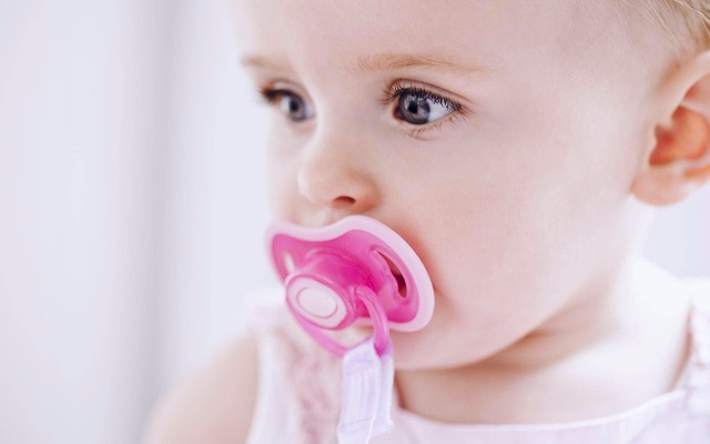 Baby with orange pacifier in his mouth with white background