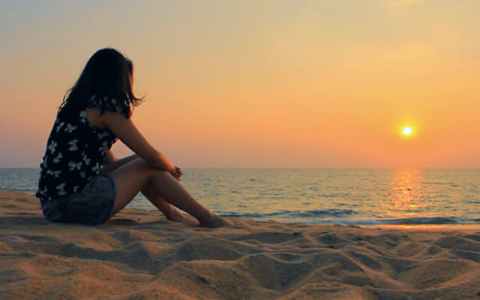 young woman sitting on the beach while the sun sets