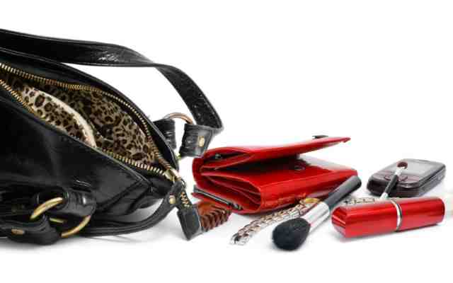 Empty black leather purse revealing wallet and other beauty accessories