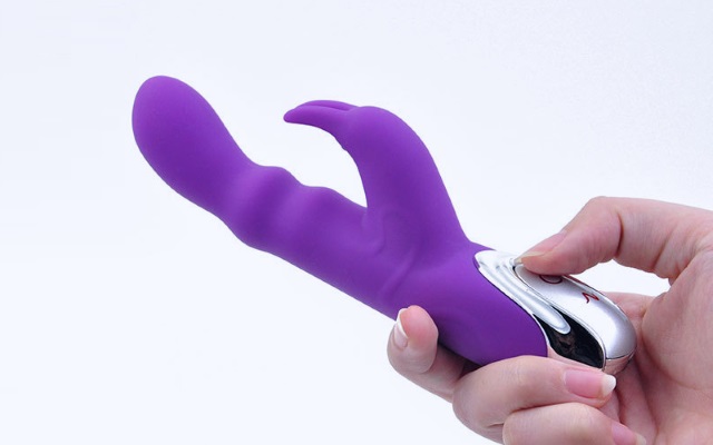 Purple silicone rabbit vibrator being held by someone with white background