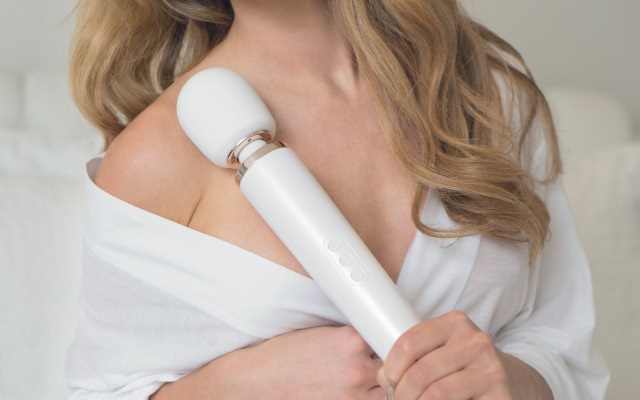 Blonde woman in white top holding up a white wand vibrator